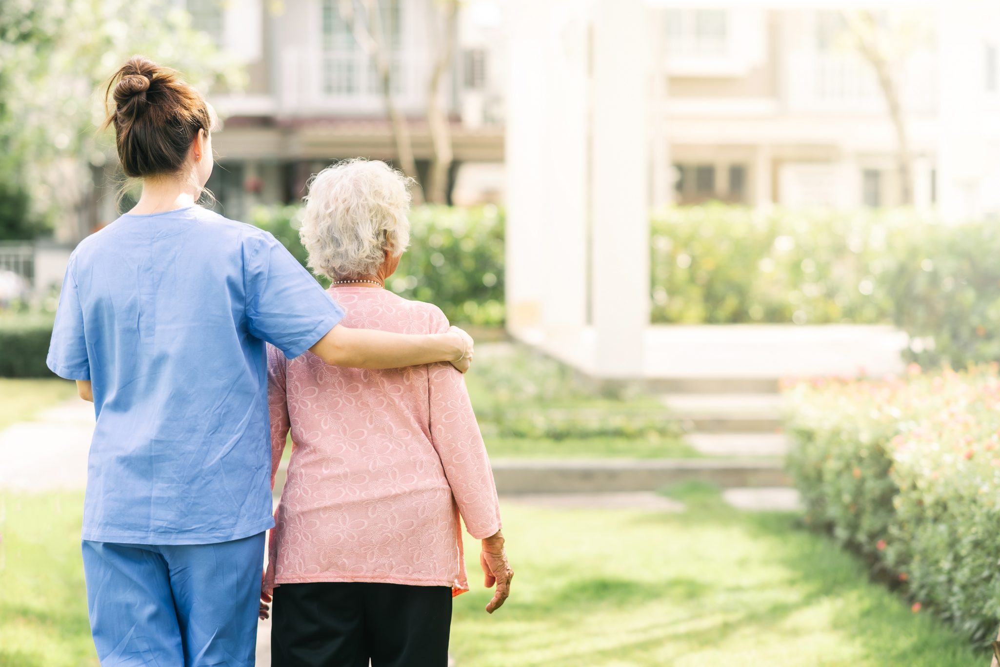 Back view of nurse caregiver support walking with elderly woman outdoor