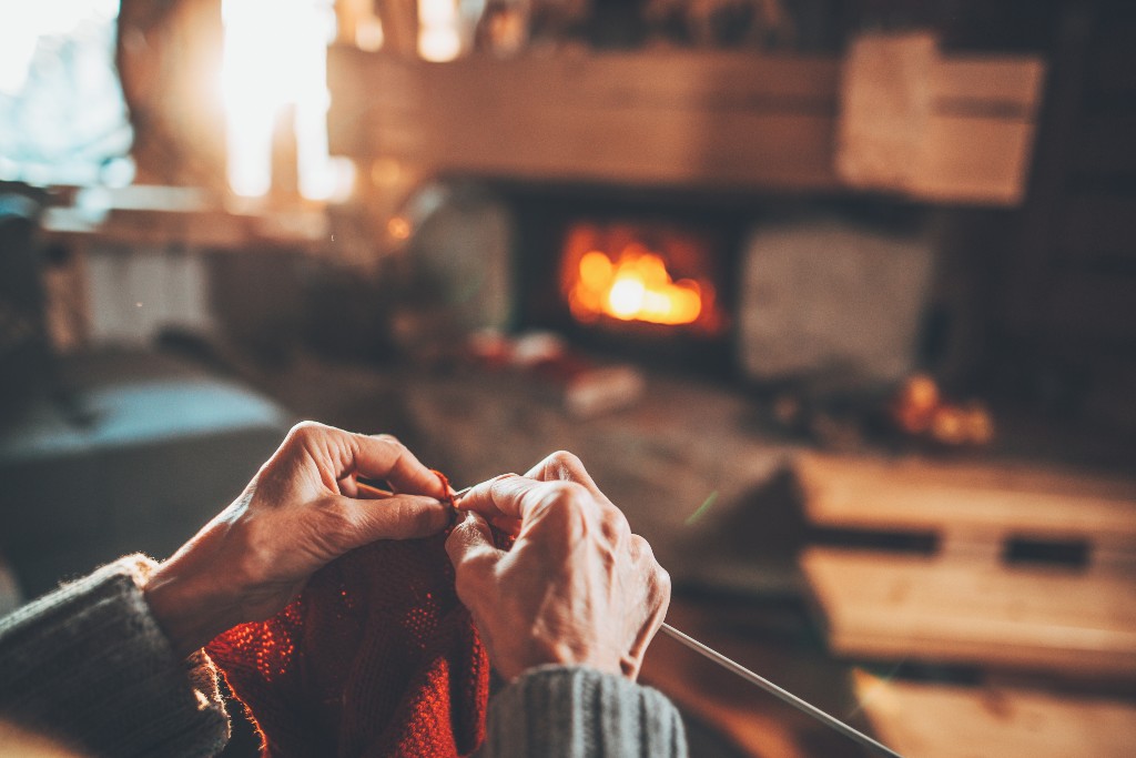 A cozy shot of an elderly woman s hands knitting with a fire going in a fireplace in the background 