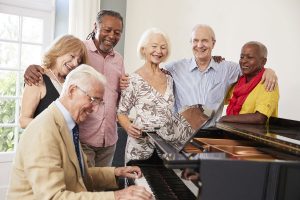 elderly seniors smiling and playing music around piano