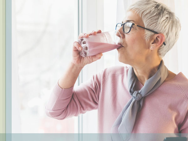 A senior woman drinks a smoothie from a glass