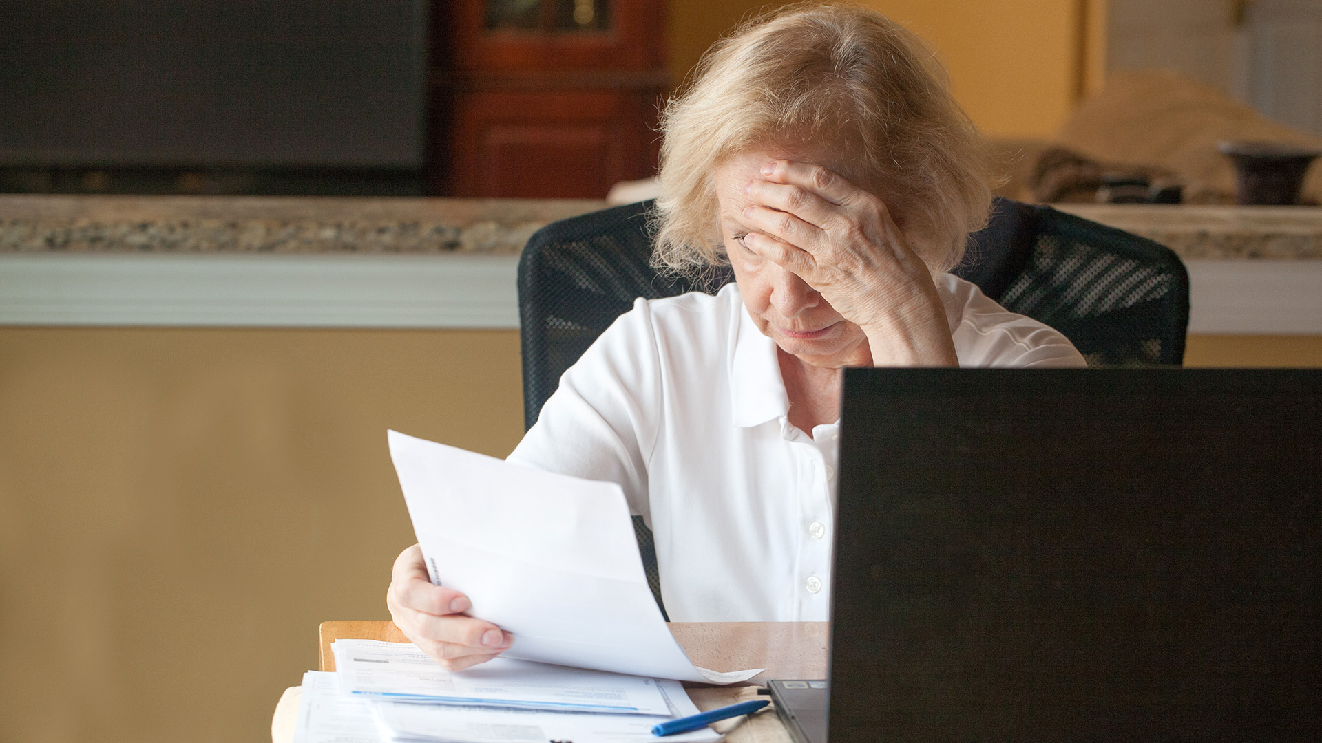 Senior woman sitting at table at home looking helpless at mounting bills