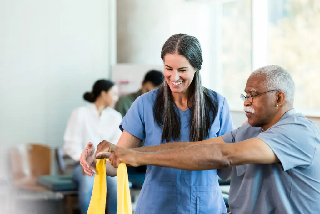 A resident discovering what is occupational therapy for seniors at Rolling Green Village in Greenville, SC. The elderly man is using a workout band with an occupational therapist.