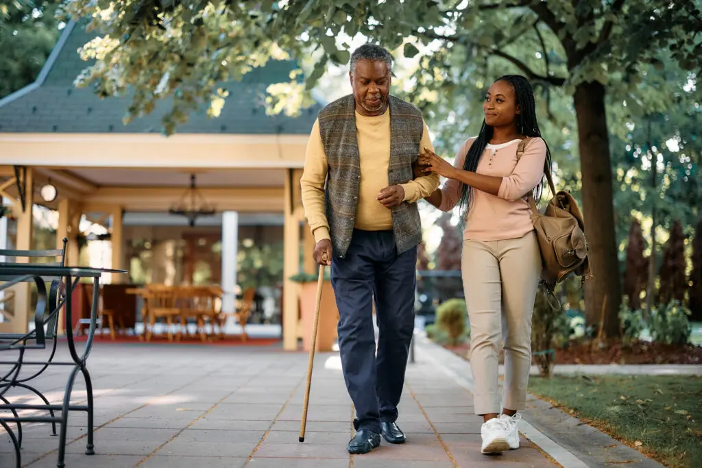 Woman helping elderly man walk and understand assisted living vs. nursing home in Greenville, SC